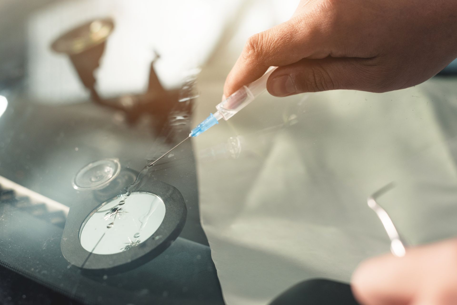 Close-up of a hands of professional windshield repairman fills a crack in the glass with a special polymer through a syringe. Elimination of cracks and chips on windshields